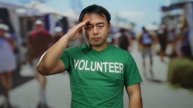 Yeşil tişörtlü genç bir adam açık hava pazarında gönüllü olarak mesaj atıyor..