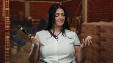 İnşaat alanında makyajdan hoşlanan bir kadın fırça ve süngerle iç mekanda beyaz üniforma giyiyor..