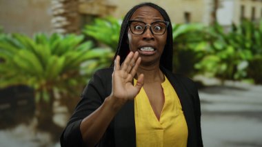 Şehir caddesinde şaşırdığını ifade eden yeşil gözlüklü ve parlak sarı gömlekli bir kadın..