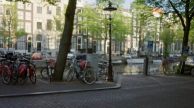 Amsterdam 'da, üzerinde bisikletler, ağaçlar ve köpek gezdiren bir kadın olan bir kanalın renksiz bir yaz atmosferi yarattığını gösteren odaksız bir sahne..