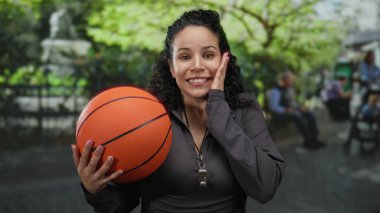 Parlak yeşillik içinde basketbol oynayan, heyecan ve neşe ifade eden bir kadın, açık hava spor koçluğu ya da eğlence aktiviteleri öneriyor..