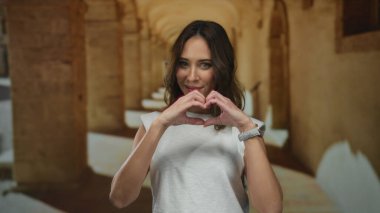 Tarihi üniversite koridorunda elleri ile kalp şeklinde gülümseyen kadın neşe ve sıcaklığı yansıtıyor..