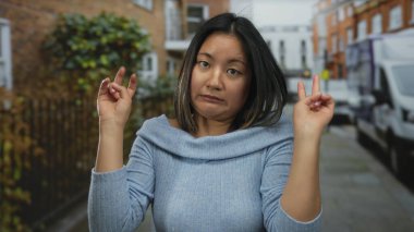 Şehir sokağında neşeli hareketler yapan genç bir kadın. Günlük süveter giyiyor. Şehrin arka planında, yeşillik ve araçlarla neşeli ve anlamlı görünüyor.