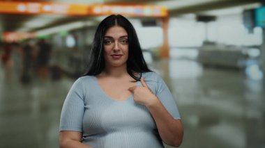 Kadın, yoğun bir havaalanı terminalinde kendini göstererek kendini inkar ediyor, meraklı olduğunu ve kapalı bir ortamda sözlü olmayan iletişim kurduğunu ifade ediyor..