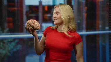 Asansörde elinde beyin mankeni olan genç bir kadın. Kırmızı bir gömlek giyiyor. Merakla gülümsüyor..