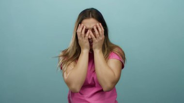 Üzüntülü bir kadın, elleri mavi arka planda, hayal kırıklığını ve endişesini ifade eden, pembe bir gömlek giyen, soyutlanmış ve duygusal, stresli ve endişeli bir kadın..