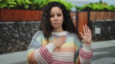 Genç İspanyol kadın, güneşli bir sokakta renkli bir kazak giyerek yemin ediyor.