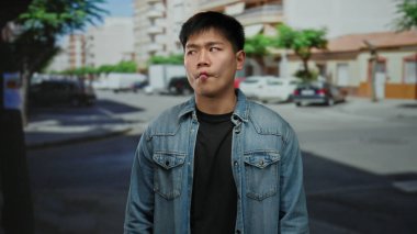 Genç adam bir şehir caddesinde komik bir yüz ifadesi sergiliyor. Arka planda binalar olan bir şehir ortamında mizah ve spontanelik sergiliyor..