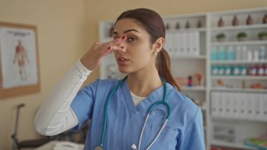 Klinik odasında steteskoplu mavi üniformalı İspanyol kadın doktor tıbbi malzemelerle çevrelenmiş vazifelerini yerine getiriyor..