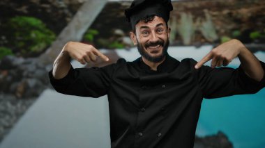 Otelde sakallı İspanyol bir aşçı, bir otelde sırıtıyor, ceketini doğal ve mavi suların arka planına gösteriyordu..