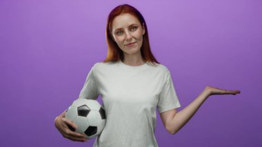 Bir kadın futbol topunu tutarken elini uzatıyor, mor bir duvara dayanıyor, beyaz bir gömlekle kızıl saçlı güzelliği sergiliyor, genç atletizmi ve çekiciliği temsil ediyor..