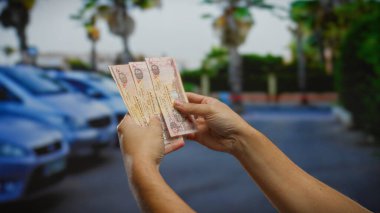 Şehir dışında, park halindeki arabaların yanında Dirham banknotları tutan adam, Uae City Caddesi 'nde bir iş anlaşması öneriyor..