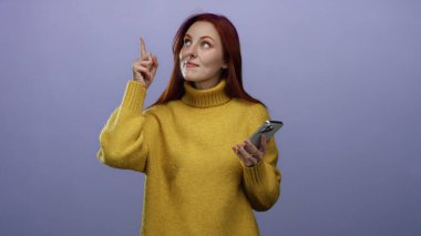 Sarı kazaklı, elinde telefon tebessümleri olan, kızıl saçlı bir kadın..