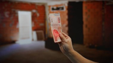 Kapalı alanda Tayvan doları tutan bir adamın el çekimi, kentsel bir inşaat sahasındaki yatırım ve finansmanı ön plana çıkarıyor.