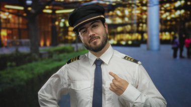 Kılavuz üniformalı genç adam, parlak şehir ışıklarının arasında liderlik sevinci ve kendine güvenini sergileyerek, geceleri kentte kendini güvenle gösteriyor..