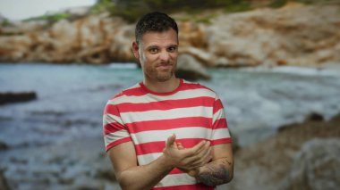 Çizgili gömlekli genç adam elleri ile bulanık bir deniz kenarı zeminine karşı, rahat ve çekici bir atmosfer taşıyor..