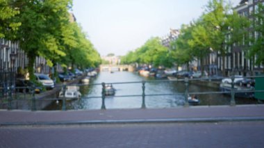 Güneşli bir günde Hollanda 'daki kentsel manzaranın dağılmış bir arka planını oluşturan yeşil ağaçlı ve tekneli Amsterdam Kanalı' nın bulanık görüntüsü.