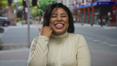 Şehir sokaklarında neşeli bir ifadeye sahip genç bir kadın, şehir arka planına gülümseyen ve el kol hareketi yapan, açık havada mutluluğu ve enerjiyi yansıtan bir kadın..