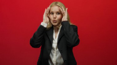 Parlak kırmızı bir arkaplan önünde peekaboo oynayan bir kadın, siyah bir takım elbiseyle karışık sarı saçlar, beklenmedik bir profesyonel ortamda oyunculuk ve entrika çağrıştırıyor..