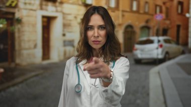 Steteskoplu İspanyol doktor kadın şehir caddesinde öfke jesti yapıyor. Şehir ortamında hayal kırıklığı ve kararlılık gösteriyor..