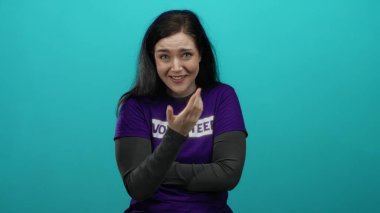 Mor gönüllü gömleğiyle mavi arka plana karşı tutkuyla şarkı söyleyen kadın, neşe ve duyguyu ifade ediyor, esmer, uzun saçlı ve elleri göğsünde.