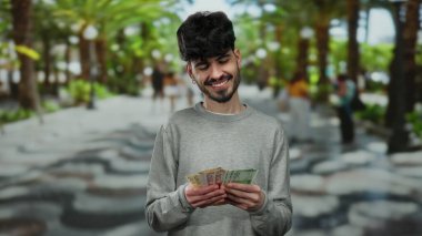 Elinde Norveç Kronu banknotları olan bir adam arka planda palmiye ağaçları olan canlı bir şehir sokağında açık hava finans teması sergiliyor..