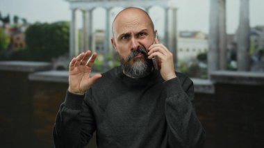 Cep telefonuyla Roma harabelerine karşı konuşan sakallı kel bir adam, endişeli görünüyor ve tarihi mekanda el kol hareketi yapıyor..
