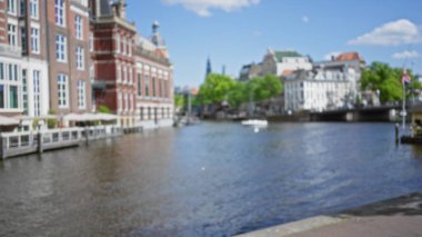 Güneşli bir günde Amsterdam 'ın ikonik kanallarının ve geleneksel mimarisinin bulanık görüntüsü, canlı renkler ve yeryüzünden silinen cazibesiyle, pitoresk şehir manzarasını yansıtıyor..