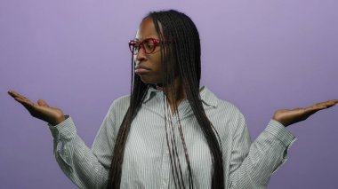 Uzun örgülü saçları ve kırmızı gözlüklü bir kadın mor bir arka plana karşı duruyor, çizgili bir gömlek giyiyor, düşünceli ve anlamlı bir tavır sergiliyor..