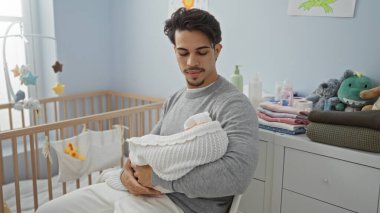 Latin kökenli genç bir adam yatak odasında bebeği kucağında tutuyor. Etrafı yumuşak oyuncaklarla çevrili. Babalık ve sevgi dolu bir ortam sergiliyor..