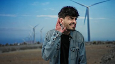 Bir tarlada el pençe divan duran genç adam mavi gökyüzünün altında yel değirmenlerinin önünde duruyor. Kot ceket giymiş, doğa enerjisini ve merakını gözler önüne seriyor..