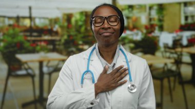 Steteskoplu kadın doktor, açık kafe terasında gündüz vakti huzur içinde gülümsediği için minnettar..