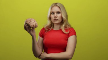 Beyni parlak sarı arka planda tutan, kırmızı tişört giyen, merak ve öğrenim gösteren bir kadın.