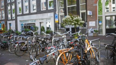 Amsterdam caddesinde park halindeki bulanık bisikletler, Hollanda 'nın şehir manzarasını vurgulayan kentsel arka planda bokeh etkisi yaratıyor..