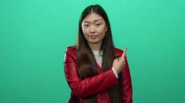 Kırmızı ceketli kadın yeşil arka planı işaret ediyor. Duygularını gösteriyor. Düşünceli, şık, çekici bir kadın..