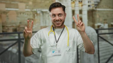 Steteskoplu bir doktor Roma harabelerinde zafer jesti yapıyor, açık havada gülümseyen genç bir beyaz adam gösteriyor, tıbbi ve tarihi unsurları birleştiriyor..