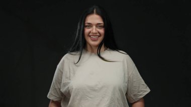İzole edilmiş siyah bir arka plan duvarına güvenle gülümseyen bir kadın, büyük beden modasını ve neşeli aurasını vurguluyor..