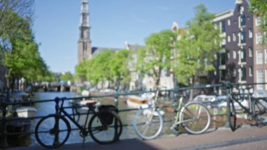 Açık mavi bir gökyüzü altında Hollanda kentsel yaşamının özünü yakalayan, odakları çözülmüş bisikletlerle Amsterdam kanallarının bulanık görüntüsü.