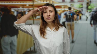 Kalabalık bir açık hava pazarında farklı müşterilerle selamlaşan bir kadın şehir yaşam tarzını ve hareketli bir sokak manzarasını sergiliyor..