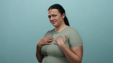 Mavi bir arkaplana karşı iğrenme hareketi yapan açık yeşil gömlek giyen, negatif duygu ve vücut dilini basit bir stüdyo ortamında sergileyen bir kadın..