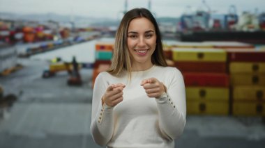 Renkli nakliye konteynırları ve deniz manzarası ile çevrili bir liman ortamında neşeli bir gülümsemeyle kameraya bakan kadın, neşe ve deniz macerasının somutlaştırıcısı..