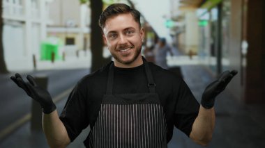 Önlük ve eldiven takan genç adam, açık havada bir şehir caddesinde, hizmetine hazır sakallı bir garson rolünü oynarken, kendinden emin bir şekilde gülümsüyor..