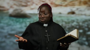 Din adamları gibi giyinmiş bir kadın deniz kenarında kitap okuyup el kol hareketleri yapıyor. Doğal arka planı olan sakin bir ortamda inanç ve maneviyatı sembolize ediyor..