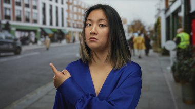 Şehir caddesinde mavi gömlekli bir kadın, meraklı ve gösterişli görünüyor, kentin hareketli ve çeşitli kültürlerini yakalıyor..