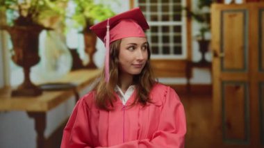 Mezuniyet elbisesi giymiş genç bir kadın, güzel dekore edilmiş bir otel odasında gururlu bir akademik başarı ve yeni bir hayata geçiş sergiliyor..