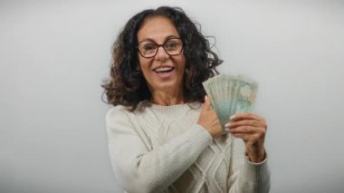 Elinde Dirham banknotlarıyla gülümseyen bir kadın beyaz arka planda başparmak işareti yaparak finansal başarı ya da tatmin öneriyor..