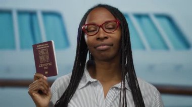 Arka planda bir tekne ile deniz kenarına yakın bir yerde Czech pasaportu taşıyan kadın, açık havada seyahat ve kimliği simgeliyor, bir limanda Afrika kökenli ve rahat giysiler sergiliyor..