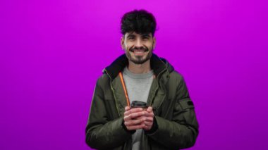 Genç adam canlı pembe bir arka plana karşı duruyor elinde bir fincan tutuyor ve sıcak bir gülümsemeyle, sıradan bir ceketle mutluluk ve tarz sergiliyor..