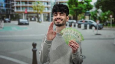Kentsel sokak ortamında elinde Rus rublesi banknotları tutarken gülümseyen bir adam coşkulu ve kendinden emin bir ifade sergiliyor..