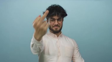 Sakallı ve gözlüklü genç adam mavi arka planda kaba bir hareket gösteriyor..